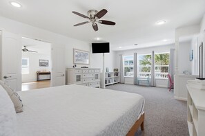 Ein Schlafzimmer mit einem Bett, einem Deckenventilator, einem Fernseher und Blick ins Freie durch eine Tür.