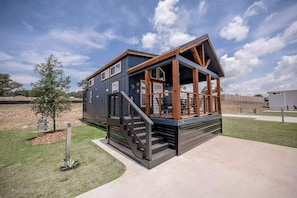 A two-story house with a covered porch and a staircase leading to the upper floor. - Luxury Tiny Home Hideaway with Resort-Style Amenities Near Fredericksburg, TX (Fredericksburg)
