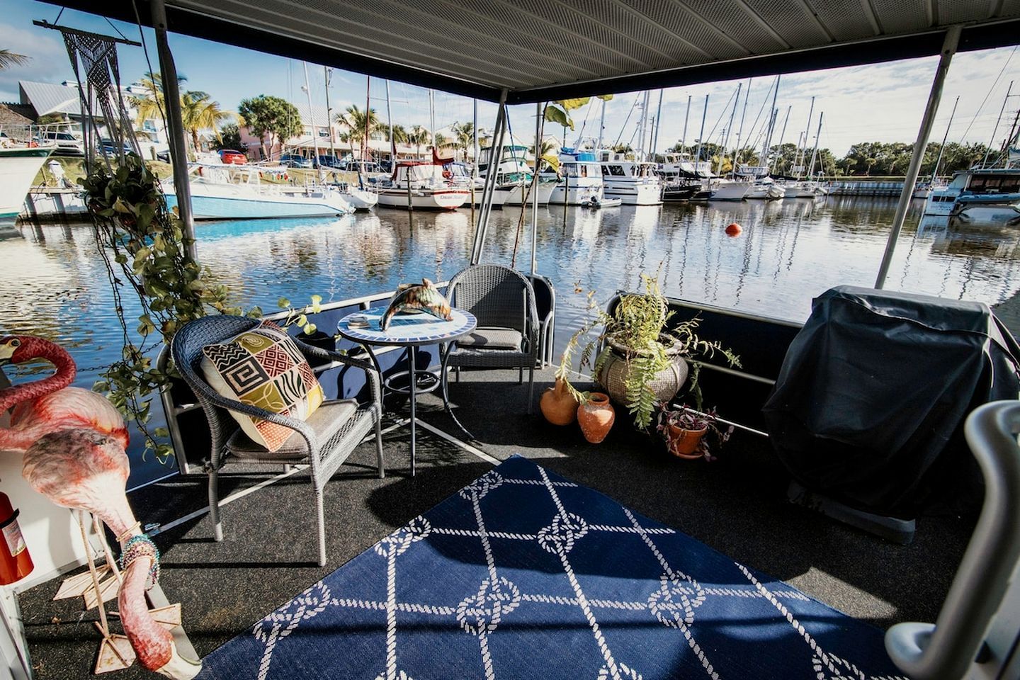 A covered outdoor seating area with a view of a marina, featuring a table, chairs, and potted plants.