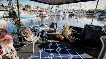 A covered outdoor seating area with a view of a marina, featuring a table, chairs, and potted plants.