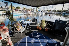 A covered outdoor seating area with a view of a marina, featuring a table, chairs, and potted plants.