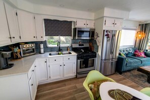 A compact RV kitchen with a stove, microwave, and refrigerator, a dining area with a table and chairs, and a sofa.