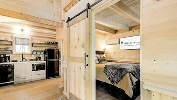 A wooden interior with a kitchen, a bed, and a sliding door leading to another room.