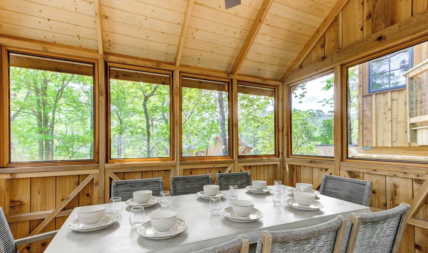 A dining area with a table set for four, surrounded by wooden walls and large windows.