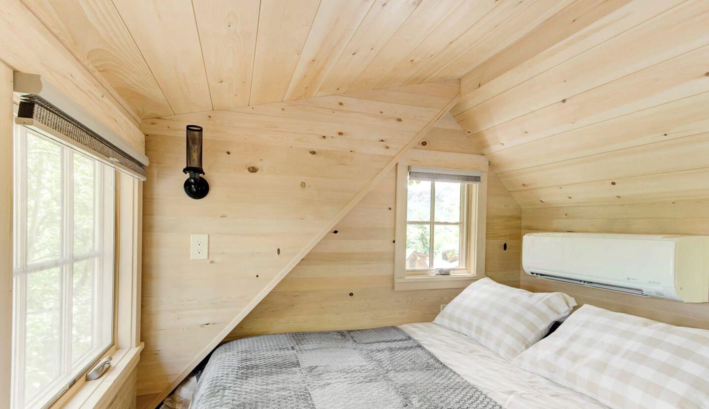 A wooden cabin room with a bed, a window, and an air conditioning unit.