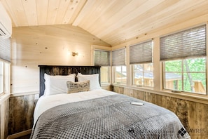 A bedroom with a wooden ceiling, a bed with white bedding, and a view of the outdoors through windows with blinds. - Luminous Tree House with Hot-tub in Gatlinburg, Tennessee (Gatlinburg)
