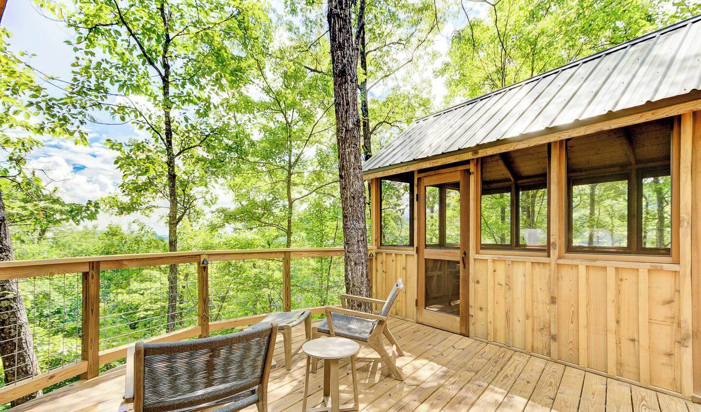 A wooden deck with wicker furniture and a metal roof, surrounded by trees.