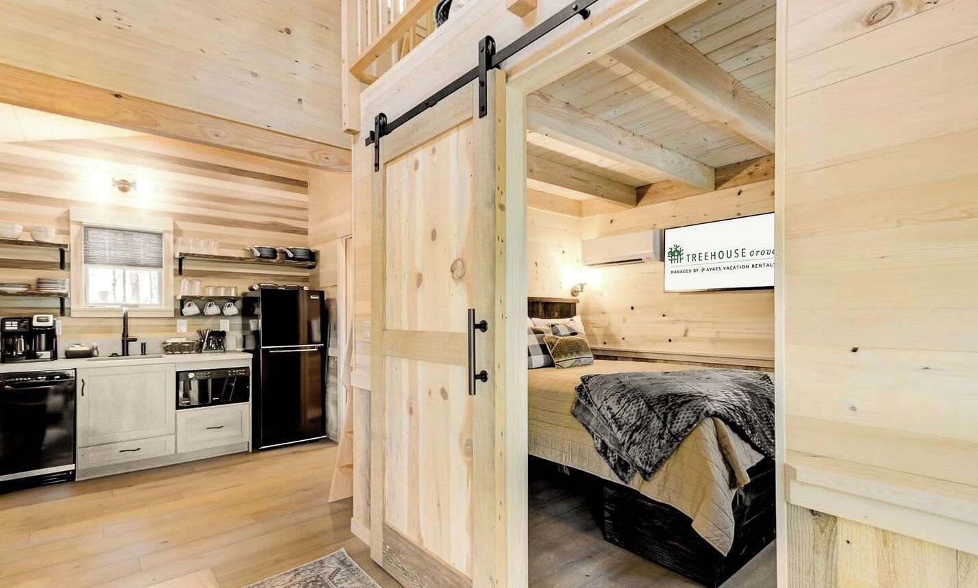A wooden interior with a sliding door leading to a bedroom with a bed and a sign indicating a vacation rental managed by a company.