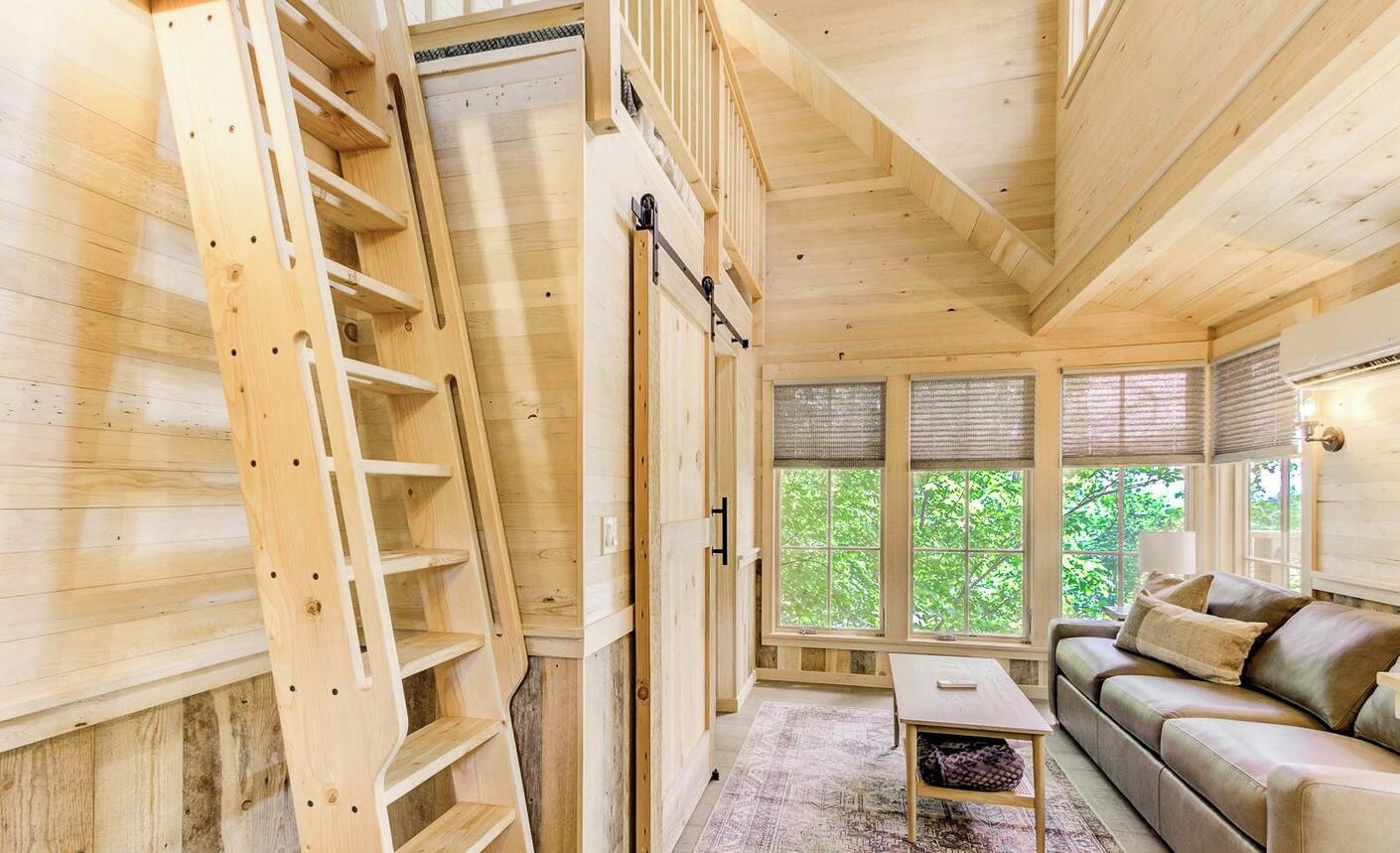 A wooden interior with a staircase, a sofa, and a window with a view of greenery.