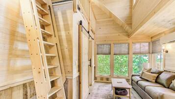 A wooden interior with a staircase, a sofa, and a window with a view of greenery.