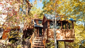 A wooden treehouse with a staircase leading up to it, surrounded by autumn foliage. - Luminous Tree House with Hot-tub in Gatlinburg, Tennessee (Gatlinburg)