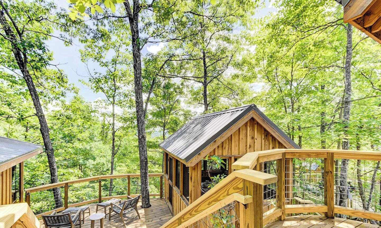 A wooden cabin with a deck, surrounded by trees.