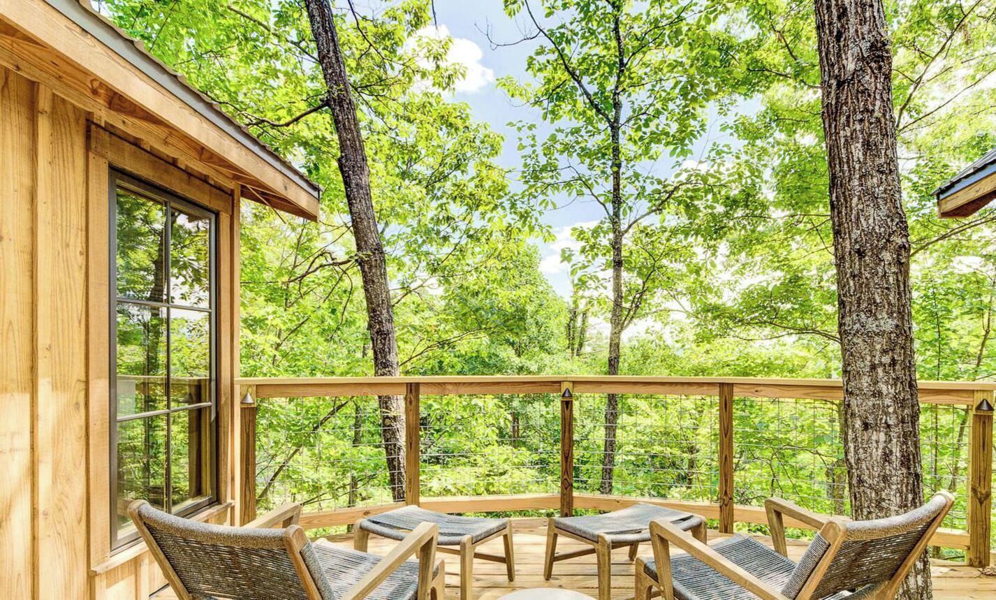 Una terraza de madera con cuatro sillas de mimbre y una mesa, rodeada de árboles.