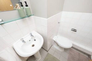 Un baño con lavamanos blanco, inodoro y repisa de vidrio con artículos de aseo.