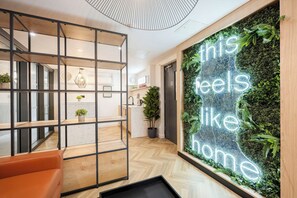 Un interior moderno con piso de madera, una zona de estar, un mostrador de recepción y una pared con un letrero verde sujeto a ella.