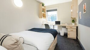 Ein Hotelzimmer mit Bett, Schreibtisch, Stuhl und einem kleinen Fenster.