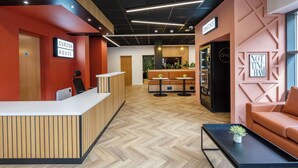 Ein moderner Empfangsbereich mit einem Holzbüro, einer Sitzecke mit Sofa und Tischen sowie einer Küche im Hintergrund.