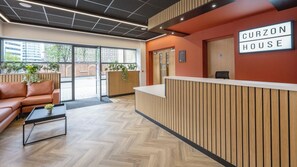 A reception area with a wooden reception desk, a leather sofa, and a herringbone-patterned floor. - Student Only Curzon House (Nottingham)