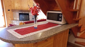 Ett kök med en bänkskiva i granit, en mikrovågsugn, en vas med blommor och en röd- och vitmönstrad bordsduk.