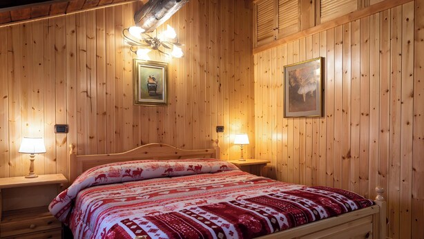 Ett rum med träpanel på väggarna, en säng, två sänglampor och två inramade tavlor.