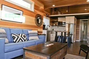 A living room with a blue sofa, a coffee table, and a kitchen area with a microwave and cabinets. - Idyllic Tiny House Rental off Scenic Byway 12 in Garfield County, Utah (Escalante)