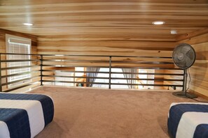 A room with two beds, a standing fan, and a window with blinds.