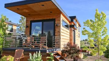 A modern wooden cabin with a covered porch, outdoor seating, and a view of the surrounding landscape.