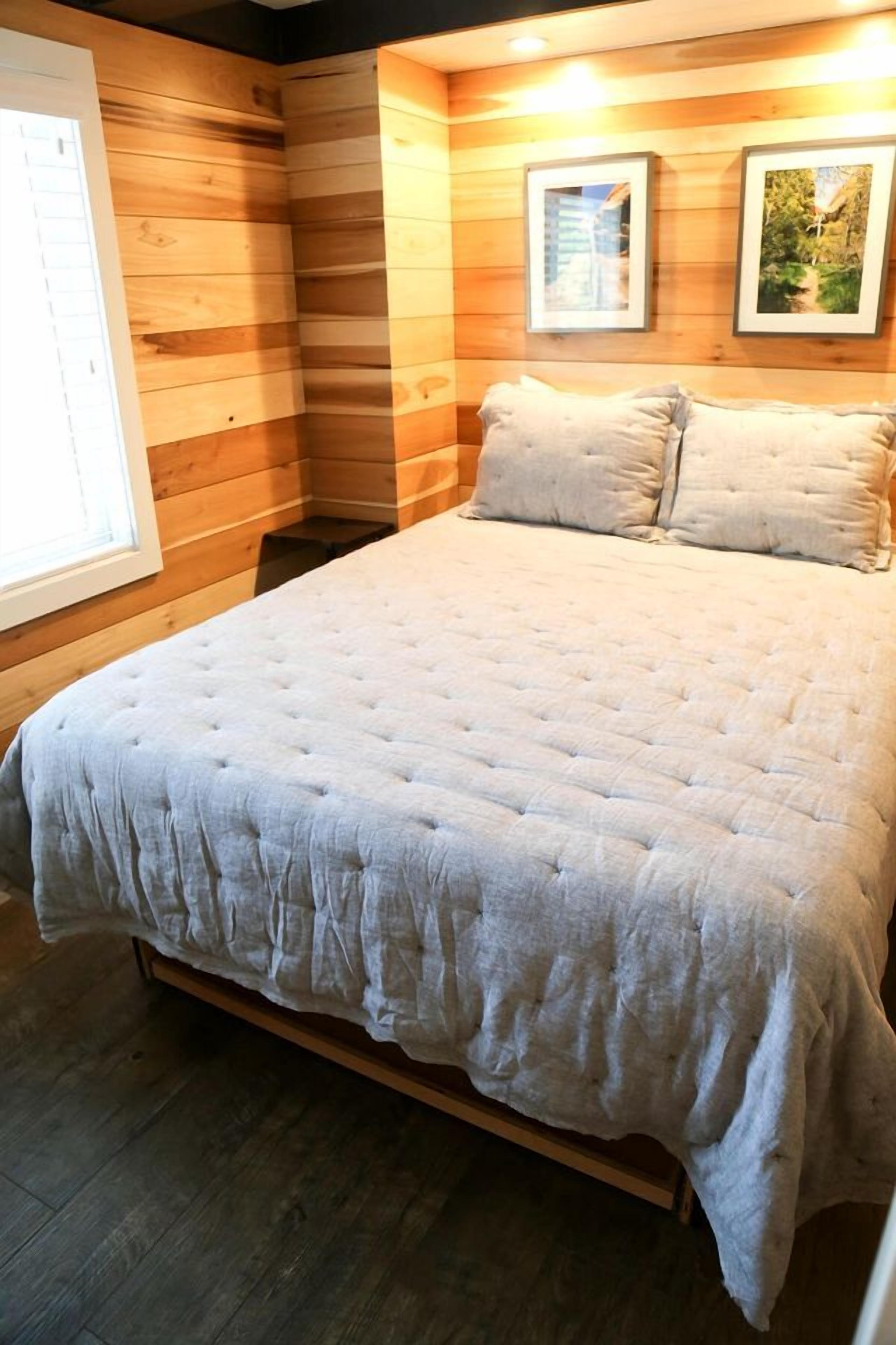A room with a large bed, wooden walls, and framed pictures on the wall.