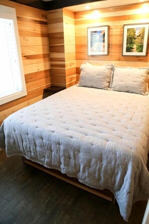 A room with a large bed, wooden walls, and framed pictures on the wall. - Idyllic Tiny House Rental off Scenic Byway 12 in Garfield County, Utah (Escalante)