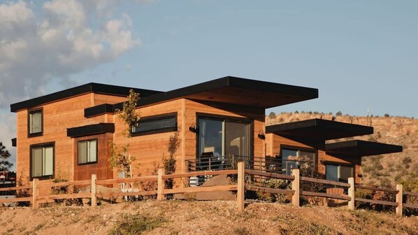 Une maison moderne à deux étages, construite en bois, avec de grandes fenêtres et une clôture en bois à l’avant.