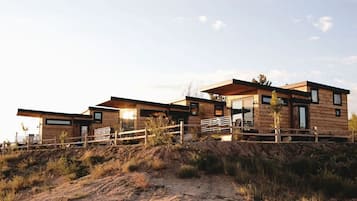 A modern wooden cabin with a deck, situated on a hillside.