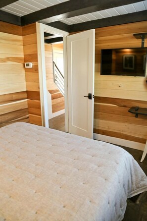 Une chambre à coucher avec un lit, une porte donnant sur un escalier et un téléviseur fixé au mur.