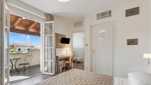 A hotel room with a bed, a desk, a chair, a television, and a sliding glass door leading to an outdoor area with a table and chairs. - Villa Carolina Rooms (Castelletto d'Orba)