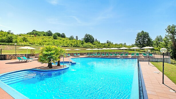 A swimming pool with a curved edge, surrounded by lounge chairs and umbrellas, set against a backdrop of greenery and a clear sky. - Villa Carolina Rooms (Castelletto d'Orba)