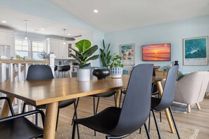 Ein moderner Essbereich mit einem Holztisch und schwarzen Stühlen, eine Küche im Hintergrund und zwei gerahmte Bilder an der Wand.