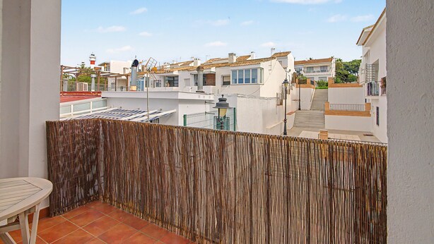 Ein Balkon mit Bambuszaun, der auf ein Wohngebiet mit weißen Gebäuden und einem klaren Himmel blickt.