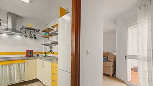 Eine kompakte Küche mit Herd, Backofen und hängenden Töpfen. Auf der Arbeitsplatte befindet sich ein Holzregal mit Geschirr und einer Kaffeemaschine.