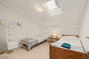 Una habitación pequeña y luminosa con una cama individual, una mesita de noche, una silla, un armario y un tragaluz.