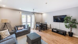 A living room with a grey sofa, a dining table with chairs, a TV mounted on the wall, and a potted plant. - Pet Friendly Family Home in New Cross with Garden (Greater London)