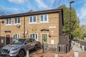 A two-story brick building with a car parked in front, a wooden fence, and a street sign indicating 'Liardet Street'. - Pet Friendly Family Home in New Cross with Garden (Greater London)