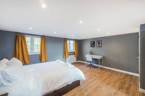A modern bedroom with a bed, two windows with curtains, a desk with a chair, and a radiator. - Pet Friendly Family Home in New Cross with Garden (Greater London)