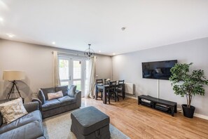 A living room with a grey sofa, a dining table with chairs, a TV mounted on the wall, and a potted plant. - Pet Friendly Family Home in New Cross with Garden (Greater London)