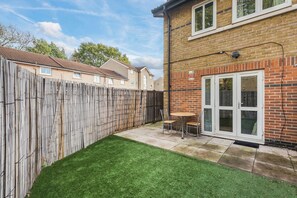 A residential backyard with a wooden fence, a lawn, and a patio area with a table and chairs. - Pet Friendly Family Home in New Cross with Garden (Greater London)