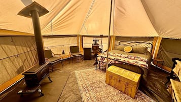A tent interior with a bed, seating area, and a wood-burning stove.