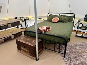 Una habitación con carpa, una estructura de cama de metal, ropa de cama verde y un baúl de madera rústico.