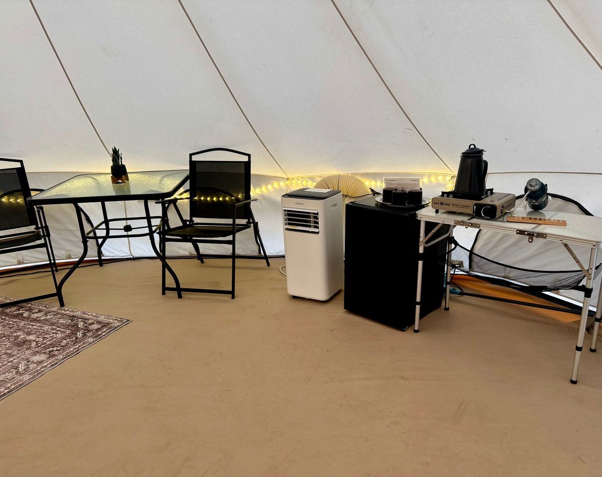 A tent with a table, chairs, a heater, a projector, and a small black cabinet.