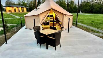 A tent with a bed inside, surrounded by a concrete patio with chairs and a table.
