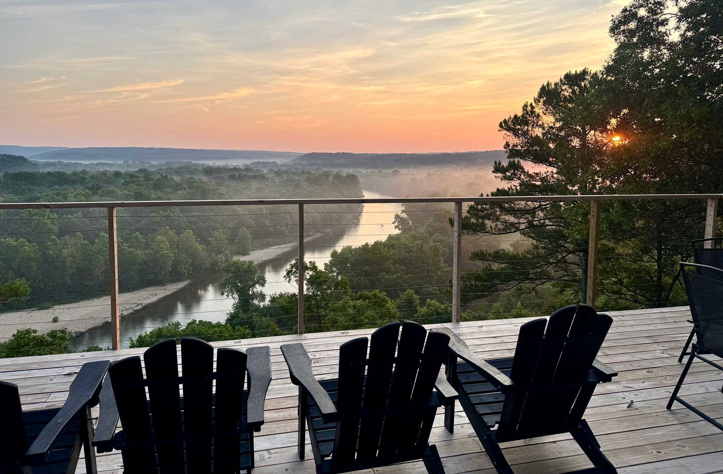 Une terrasse avec des chaises donnant sur une rivière et des collines boisées.