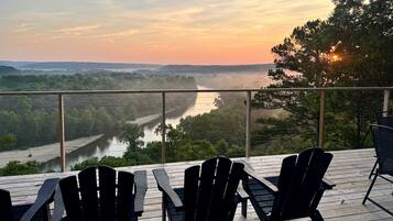 Une terrasse avec des chaises donnant sur une rivière et des collines boisées.