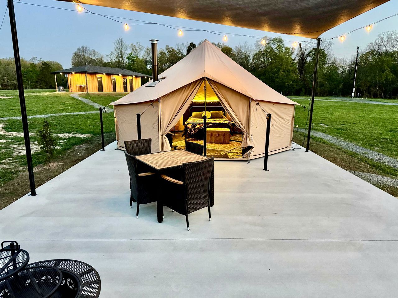 Een tent met een bed aan de binnenkant, een tafel en stoelen buiten.